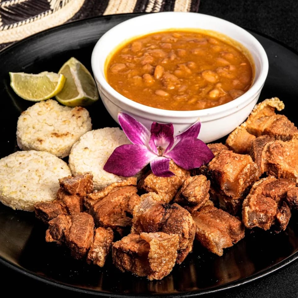 Mendoza's Colombian Cafe's bandeja paisa with chicharron, arepas, beans, lime, and a purple orchid.