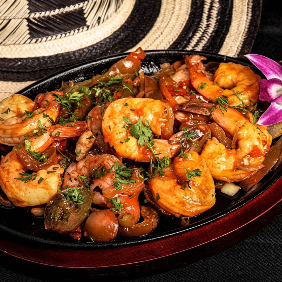 Sizzling shrimp fajitas with peppers and onions, garnished with parsley, on a black skillet.