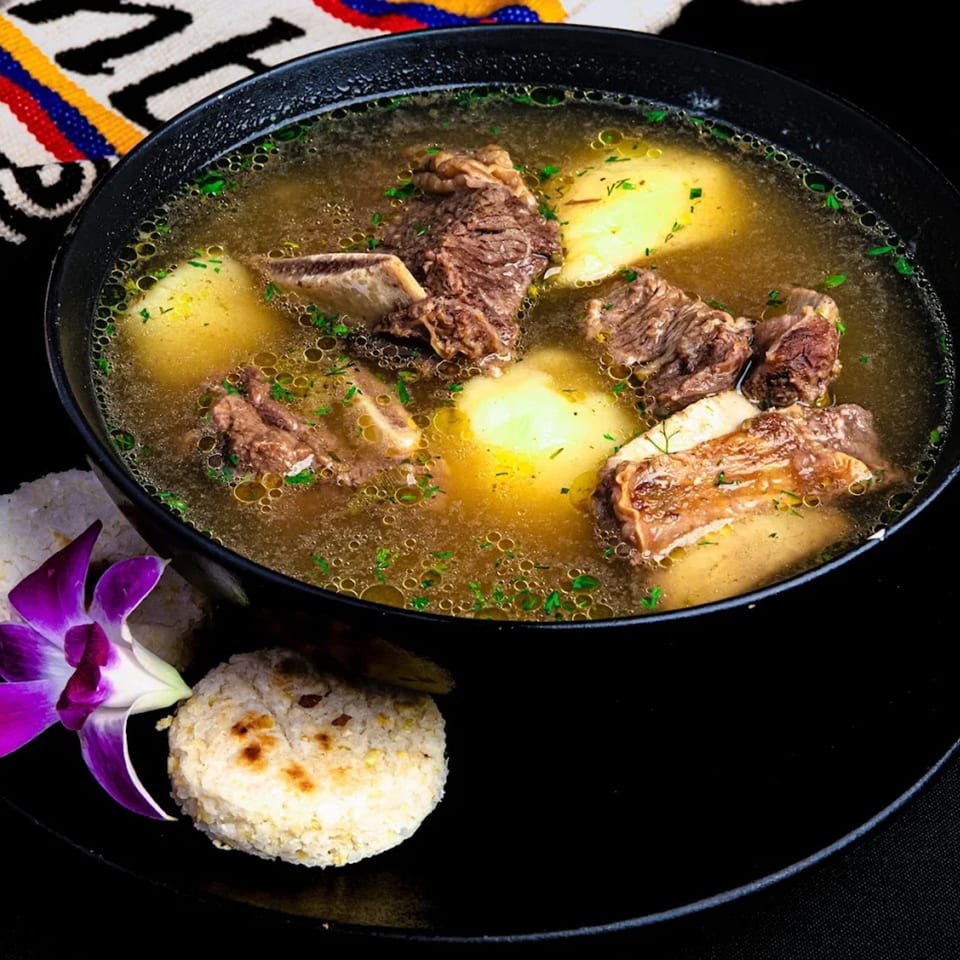 Hearty Colombian beef rib soup with potatoes, garnished with parsley, served with rice and an arepa.