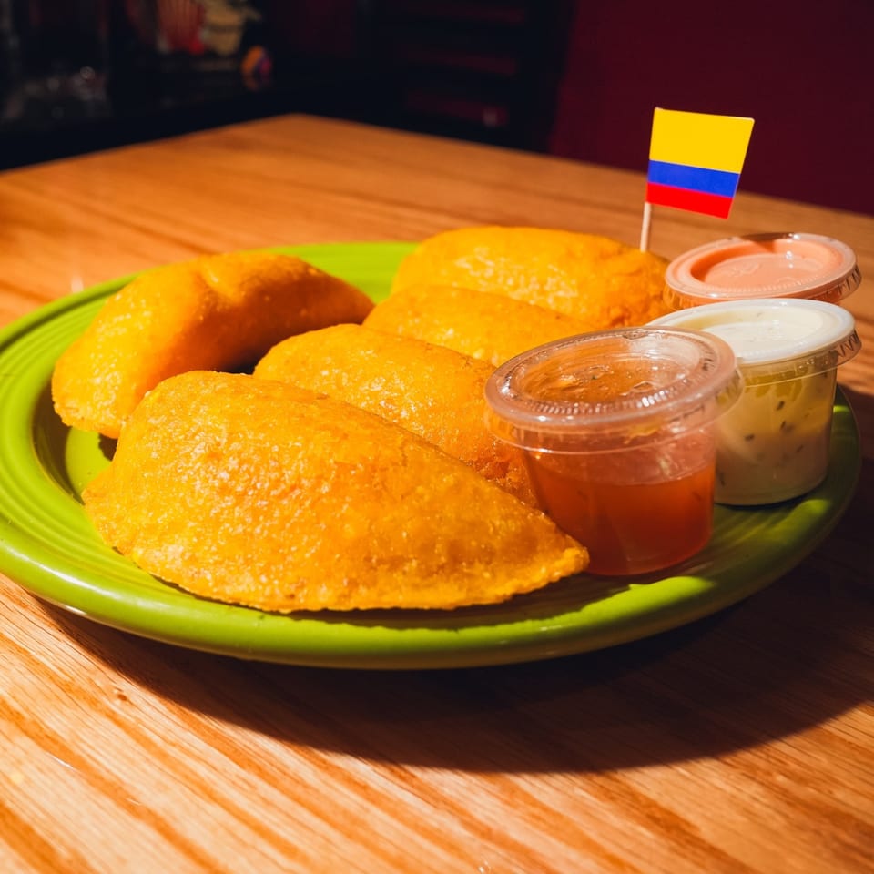 Golden Colombian empanadas on a green plate with dipping sauces and a Colombian flag toothpick.